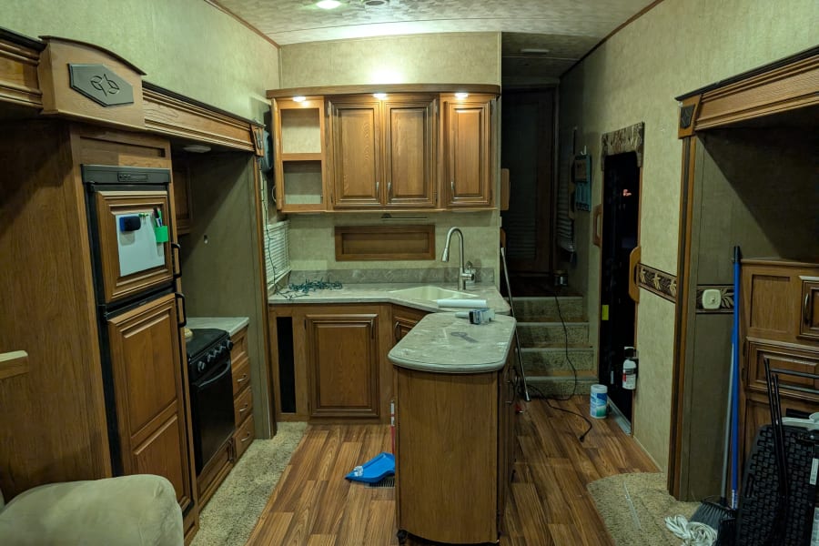 This RV rental features a cozy kitchen with wood cabinets, sink, stove, fridge, and island, perfect for mobile living.