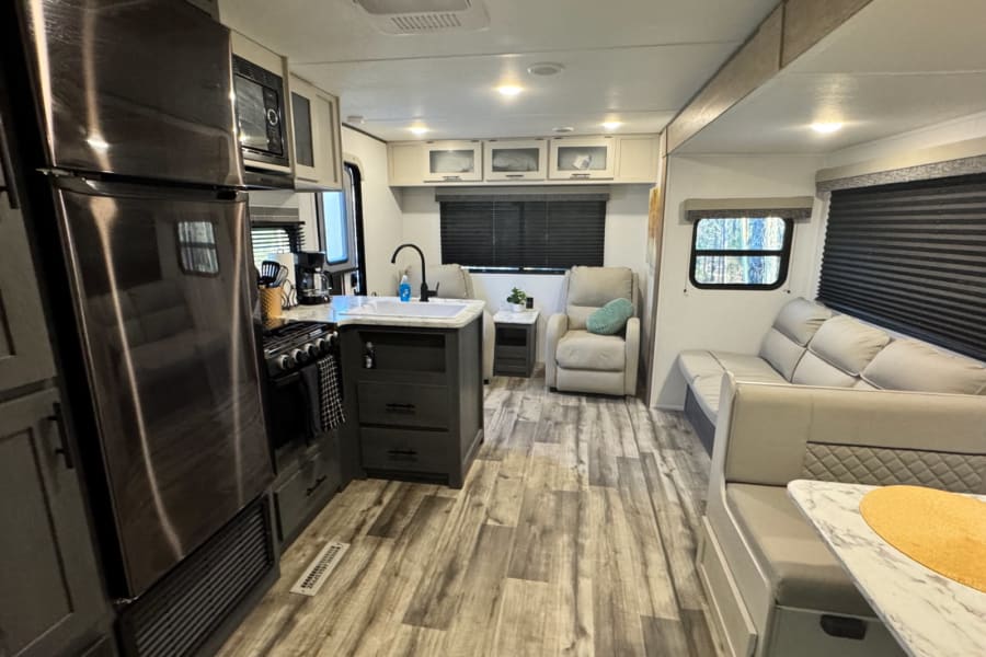 Explore this clean and modern RV rental's inviting interior, featuring a full kitchen, comfortable living, and dining space.