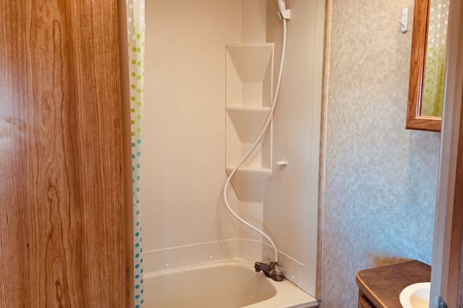 Inside an RV rental bathroom, featuring a compact shower, toilet, and wooden vanity with sink. Practical and functional space.