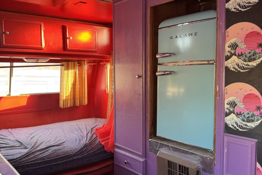 Vibrant retro RV rental interior featuring a light blue Galanz fridge, red accents, purple walls, and Hokusai-style art.