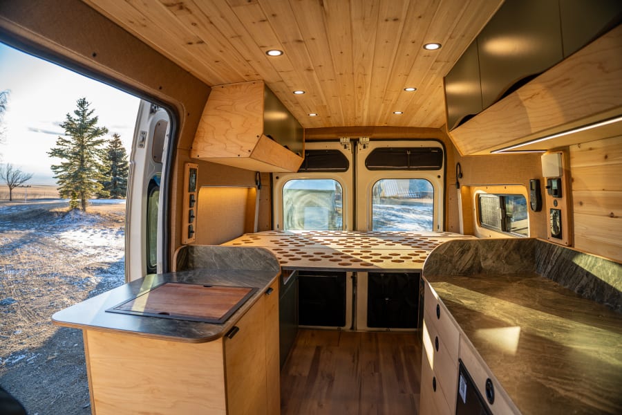 Spacious RV rental interior with custom wood build, integrated kitchen, bed, and scenic nature views from the back.