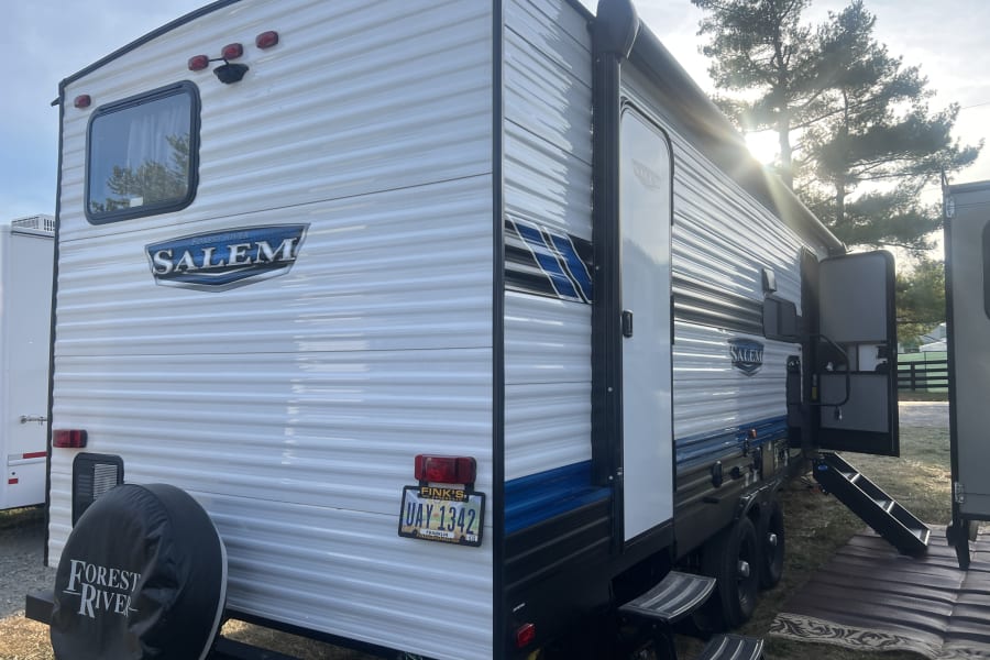 Forest River Salem RV rental parked outdoors, showcasing its side entrance, awning, and rear tire.