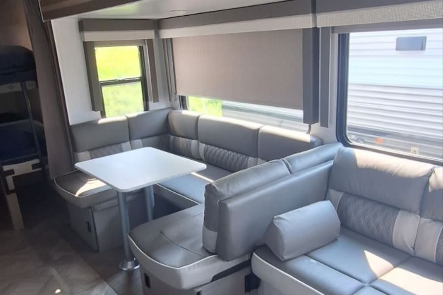 Comfortable rv rental interior with a gray U-shaped dinette, central table, and visible bunk beds for travel comfort.