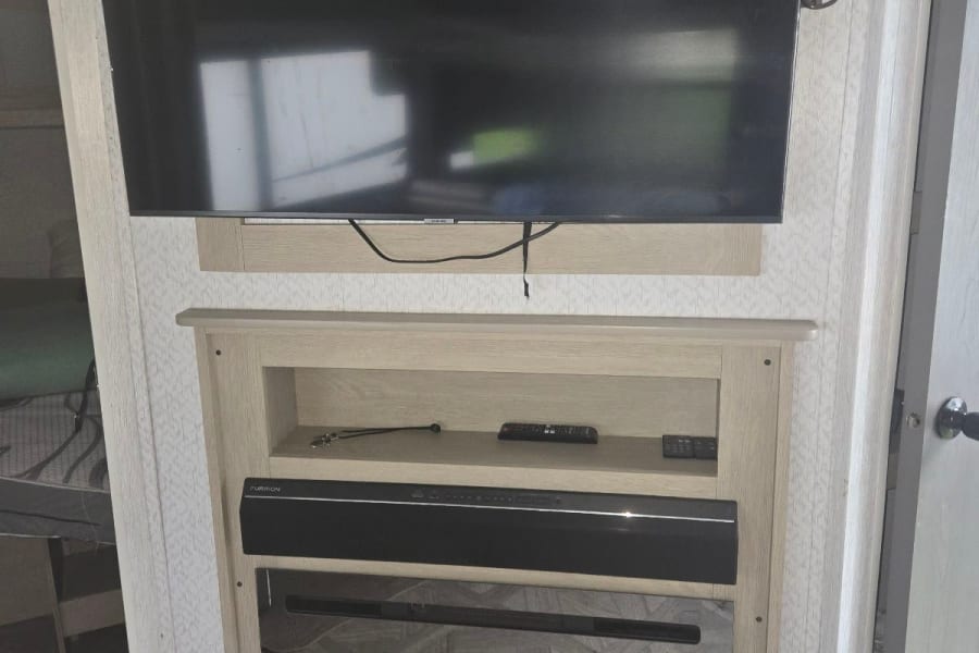 Modern RV rental interior with a wall-mounted TV, built-in media console, soundbar, and electric fireplace.