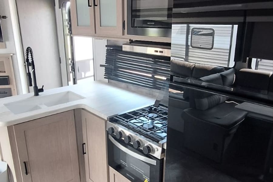 RV rental: Modern kitchen featuring black appliances, light wood cabinets, double sink, and patterned floor.