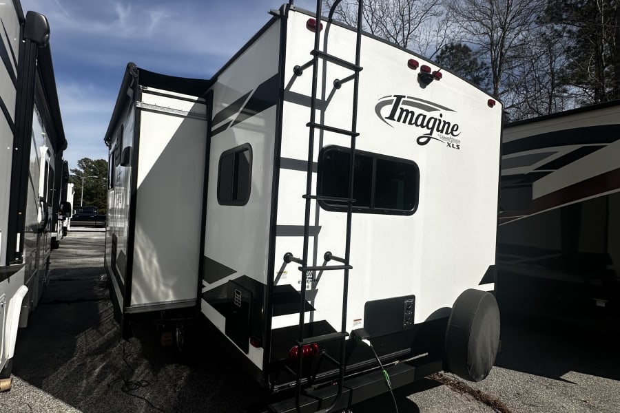 Rear view of a white Grand Design Imagine XLS travel trailer in a parking lot, powered up and ready for RV rental.