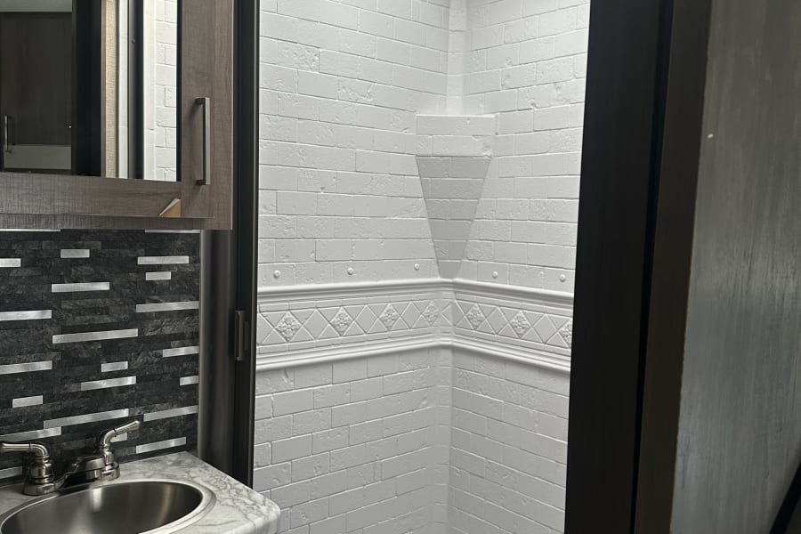 Step into this modern RV rental bathroom! It boasts a clean shower with textured walls, a vanity, and a mirror.