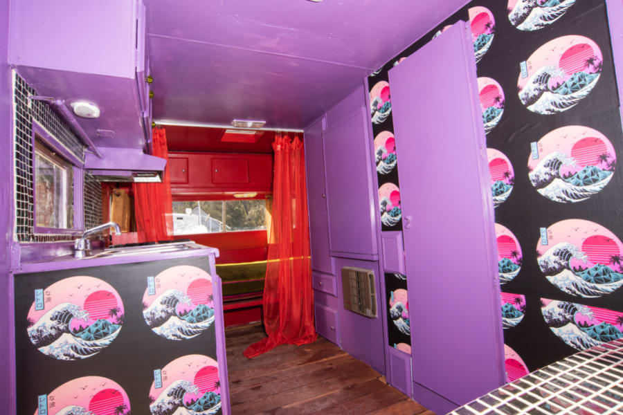 Step into this unique purple & red vaporwave RV rental interior. Features a kitchen, artistic wave panels, and eclectic decor.