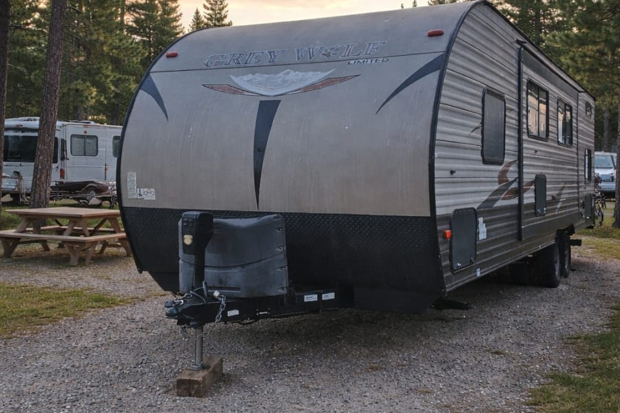 Grey Wolf RV rental at a scenic campground. Ready for adventure amidst tall pine trees at sunset, perfect for camping trips.