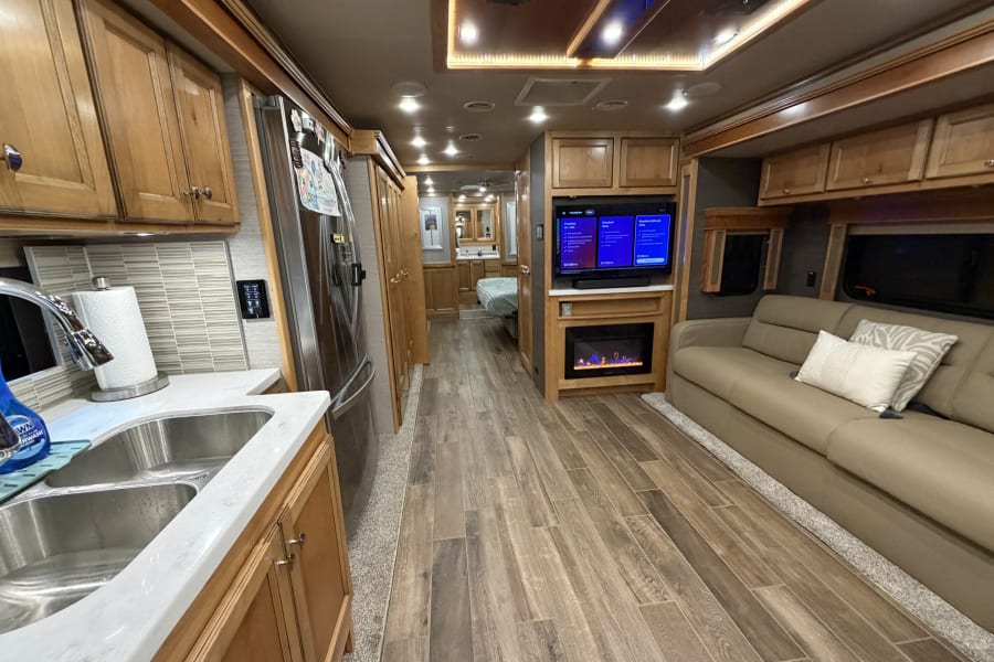 Modern rv rental interior: bright kitchen with sink, full fridge, comfy living space with TV & fireplace. Perfect for your journey.