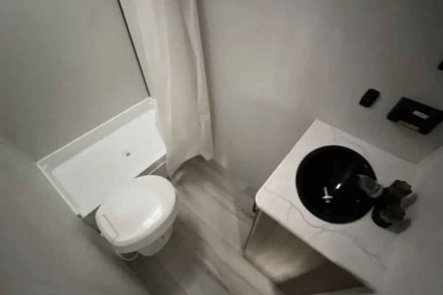 This RV rental bathroom offers compact convenience with a toilet, shower, and modern black sink vanity. Perfect for travel!