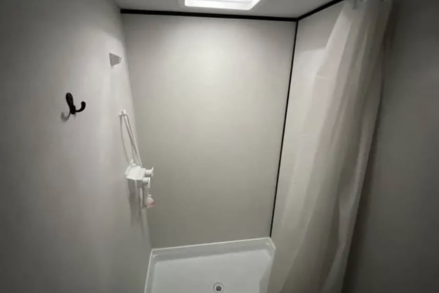 RV rental shower: compact, with white pan, curtain, wall-mounted shower head, hooks, and ceiling light.