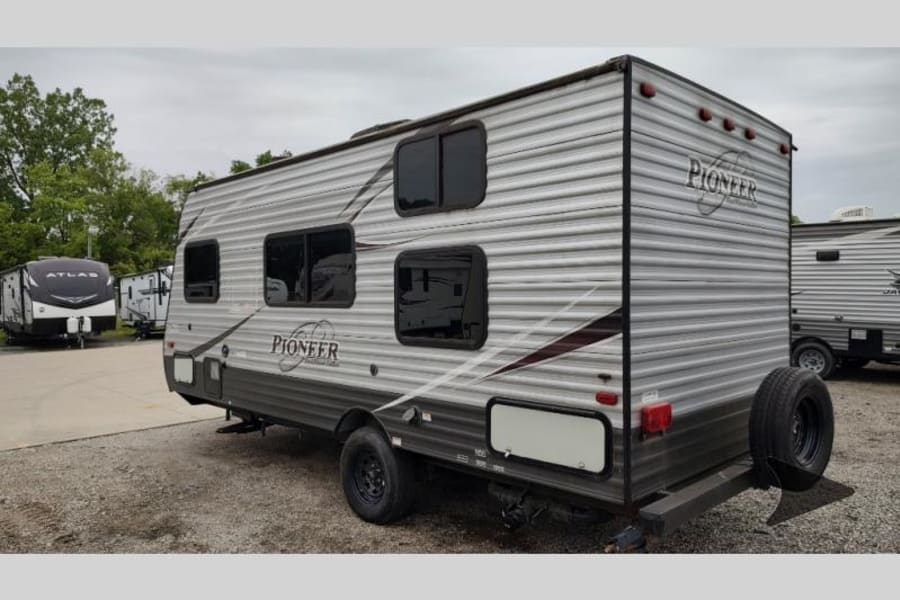 A gray Pioneer travel trailer, perfect for an rv rental, shown from the rear-side in a lot with other RVs.