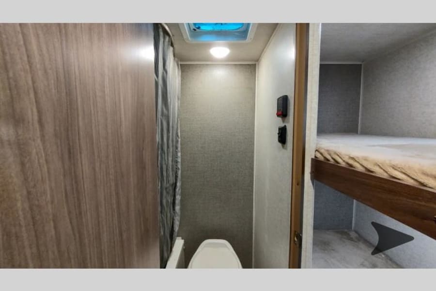 Inside an RV rental: compact bathroom with toilet and shower curtain, next to a bunk bed for extra sleeping space.