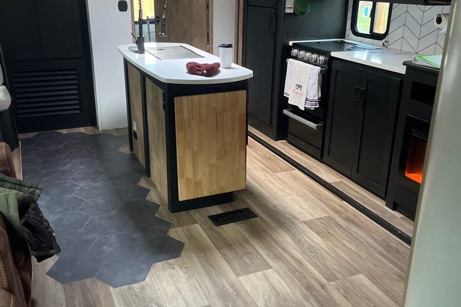 Modern RV rental interior: Stylish kitchen with island, black cabinets, and unique mixed wood/hex tile flooring.