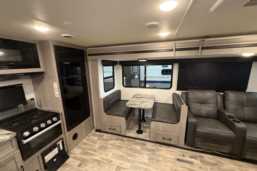 View inside an RV rental showing a modern kitchen, compact dinette area, and comfortable reclining chairs.