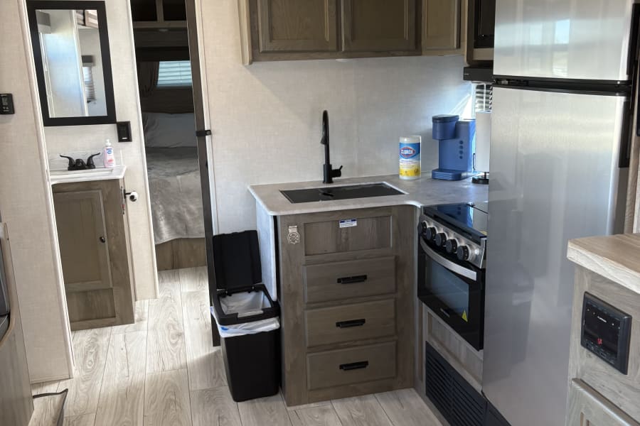Well-appointed RV rental interior: modern kitchen with stove, fridge, sink; bathroom & bedroom seen down the hall.