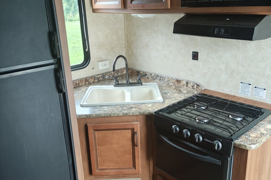 This RV rental kitchen features a black refrigerator, double sink, microwave, and a 3-burner stove/oven combo with wood cabinets.