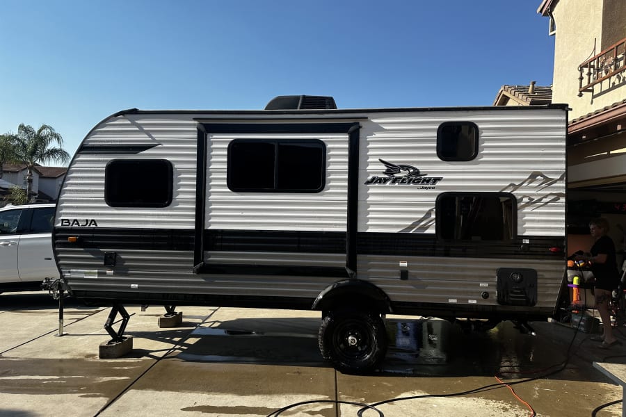 Preparing a Jay Flight Baja travel trailer for an rv rental, undergoing exterior washing and maintenance on a sunny day.