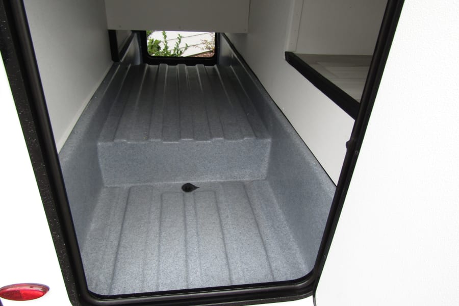 Spacious, clean RV rental storage compartment with a textured, step-up floor and drain, ideal for gear.