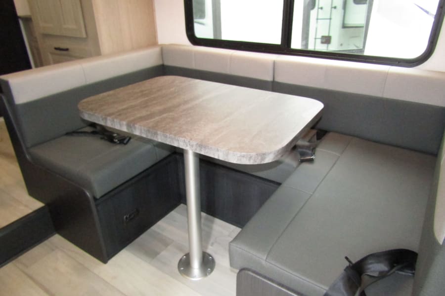 Cozy RV rental dinette with gray booth seating, a light-colored table, and a large window.