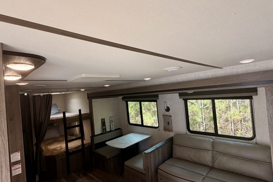 Spacious rv rental interior features bunk beds, dinette, sofa, and a kitchen area, offering comfortable living with nature views.