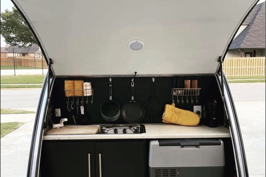 This RV rental's compact kitchen boasts a stove, sink, fridge, & storage, perfect for outdoor cooking & camping convenience.