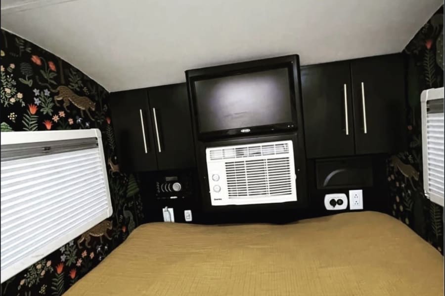 Cozy RV rental bedroom with dark jungle wallpaper, TV, AC, and a comfy mustard bed. Perfect for travel adventures!