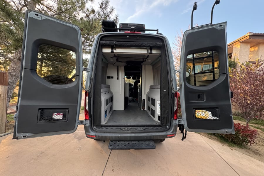 Spacious rear interior of a gray custom camper van with both back doors open, revealing modular storage units. Ideal for rv rental adventures.