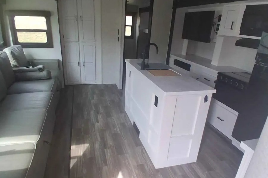 Bright RV rental with a contemporary kitchen island, gray sofa living space, and light wood flooring.