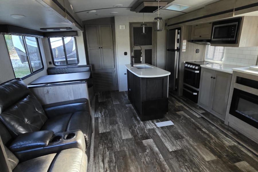 Spacious RV rental interior with modern kitchen, dinette, recliners, and fireplace. Perfect for travel adventures.