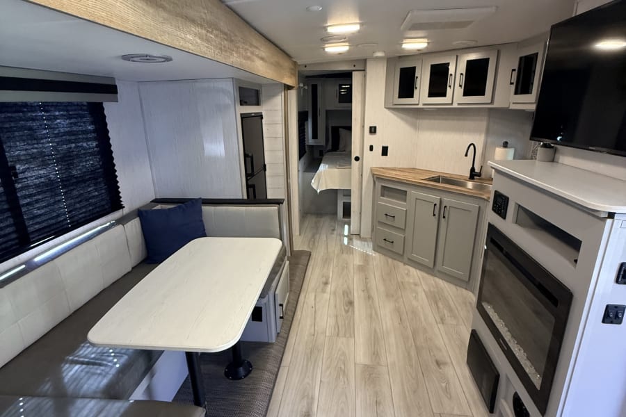 Modern rv rental interior with a cozy dinette, well-equipped kitchen, and an inviting fireplace for comfortable travels.