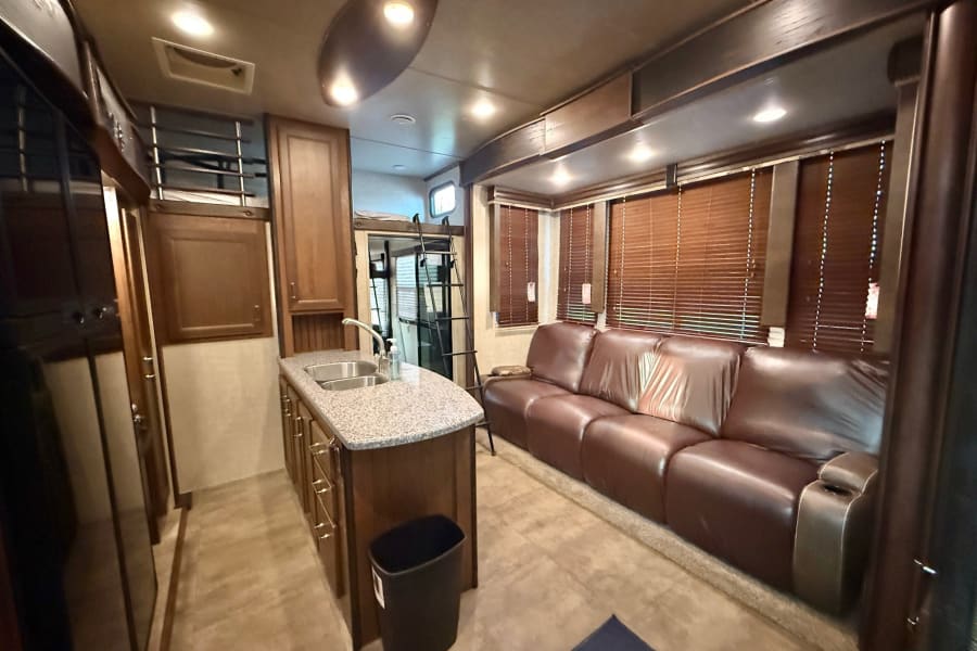 Spacious RV rental interior featuring a modern kitchenette, comfortable brown leather sofa, and bunk beds. Perfect for family adventures.