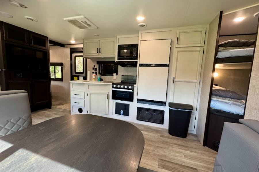 Spacious rv rental interior showcasing a full kitchen, dining area, and comfy bunk beds. Modern travel trailer comfort.