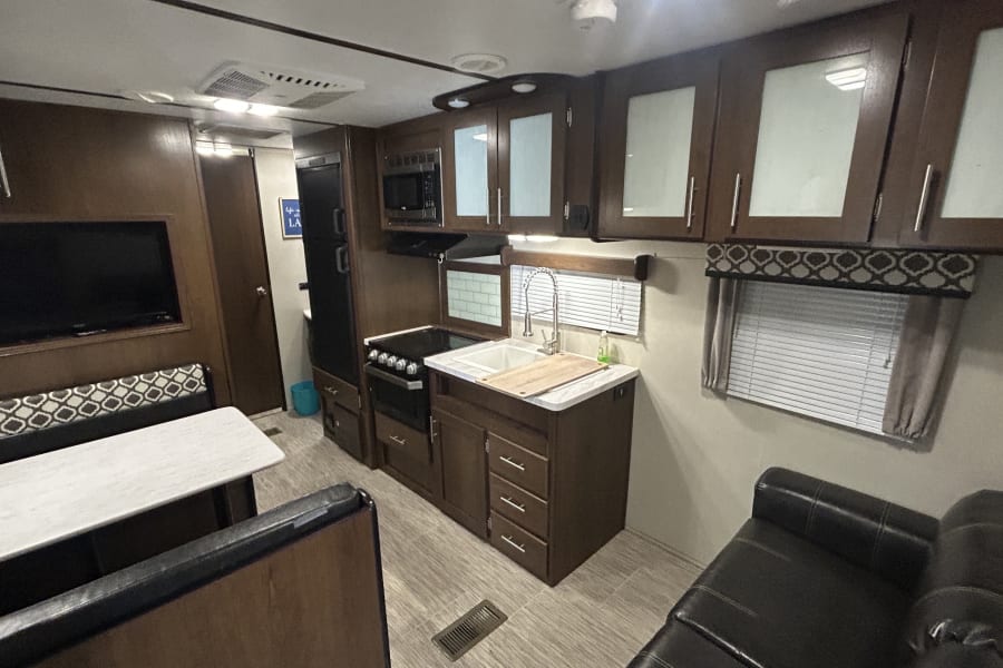 Spacious RV rental interior featuring a kitchen with microwave/stove, dining area, sofa, TV, and wood-look finishes.