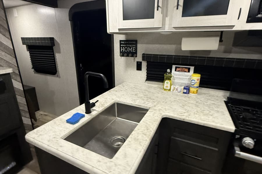 Modern RV rental kitchen features a sink, black faucet, stove, and ample cabinet space with cleaning essentials.