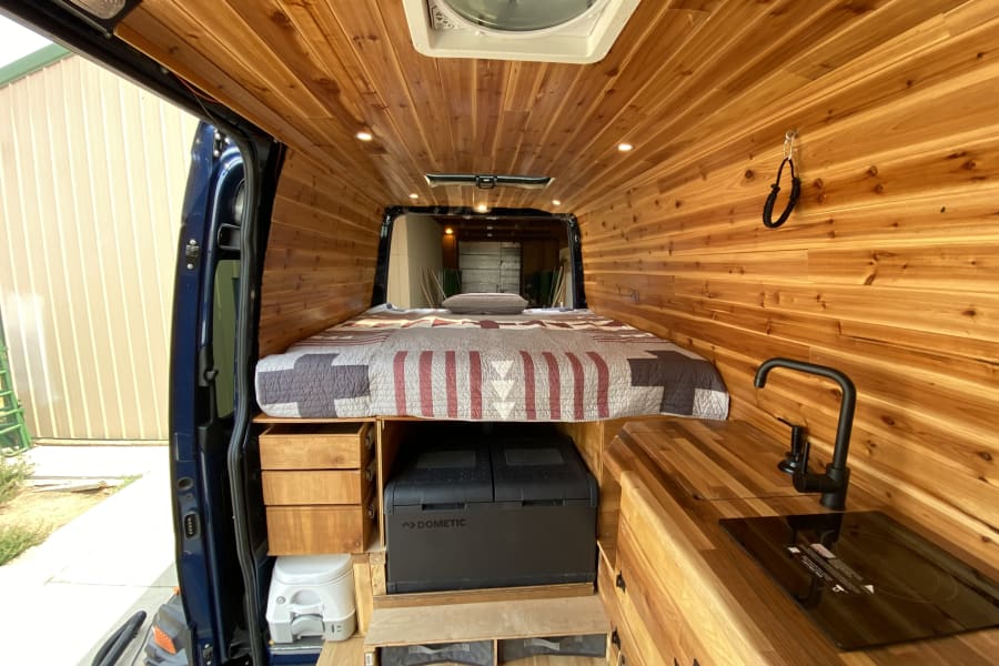 RV rental ready: Beautifully crafted camper van interior with wood paneling, bed, kitchen, Dometic fridge, and toilet.