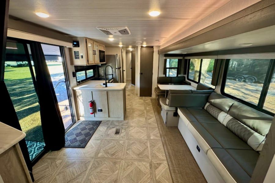 Inviting RV rental interior: modern kitchen, dining booth, and long sofa in a bright living space with outdoor views.