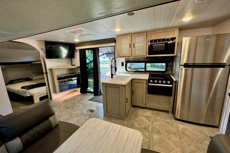 Modern RV rental interior: kitchen, bunk beds, living space, TV, and fireplace. Enjoy comfort on the road.