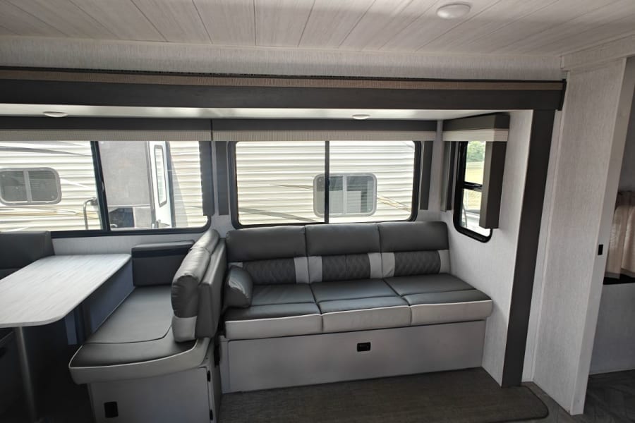 Modern RV rental interior with a dinette, comfortable sofa, large windows, ceiling AC, and stylish patterned flooring.