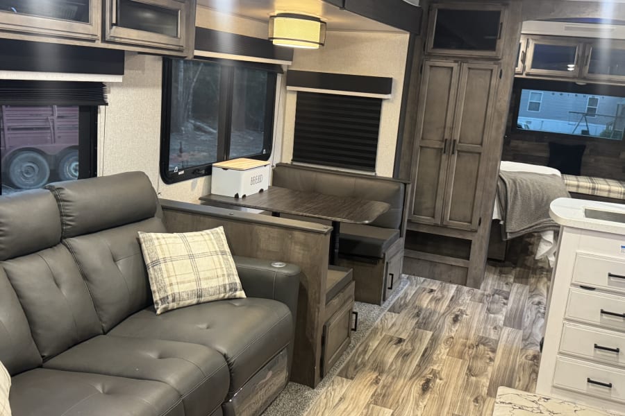 Cozy rv rental interior: dark sofa, dinette, wood-look floor. A comfortable and well-appointed space for your adventures.