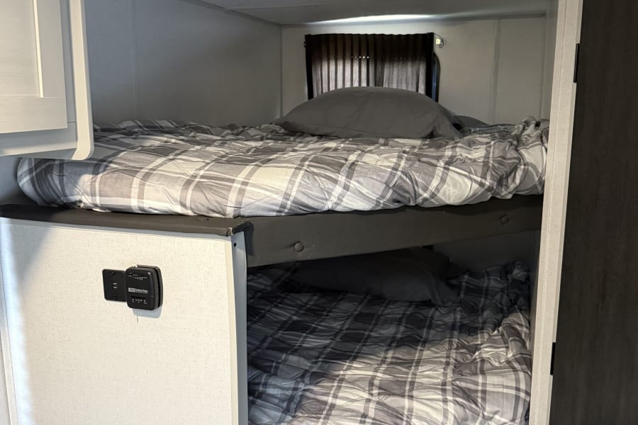 Cozy RV rental bunk beds with plaid bedding, featuring a thermostat on the lower bunk's side panel.