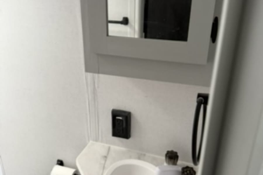 Clean RV rental bathroom vanity featuring a white sink, mirrored cabinet, and toilet paper holder.