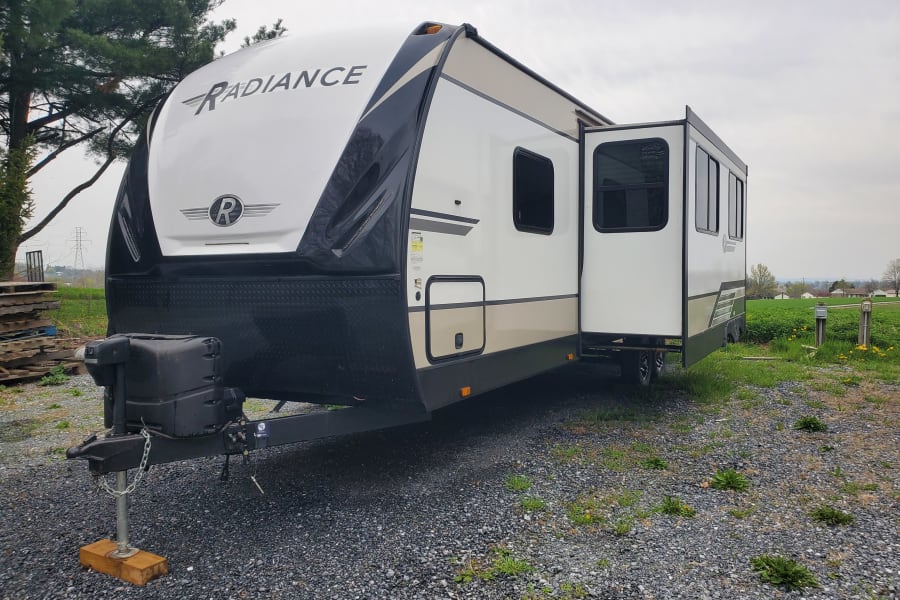 This Radiance travel trailer, an RV rental, is parked on gravel with its slide-out extended, ready for your next adventure.