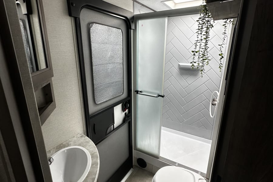 Explore this clean RV rental bathroom, offering a compact sink, toilet, and shower with modern gray herringbone tiles and a skylight.