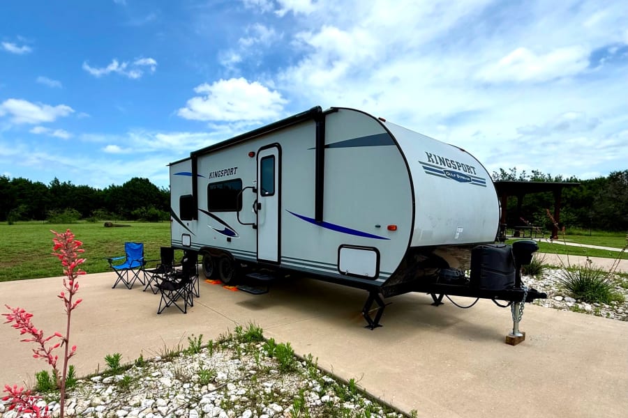 A Kingsport travel trailer RV rental is parked at a serene campsite with chairs, ready for a peaceful camping getaway.