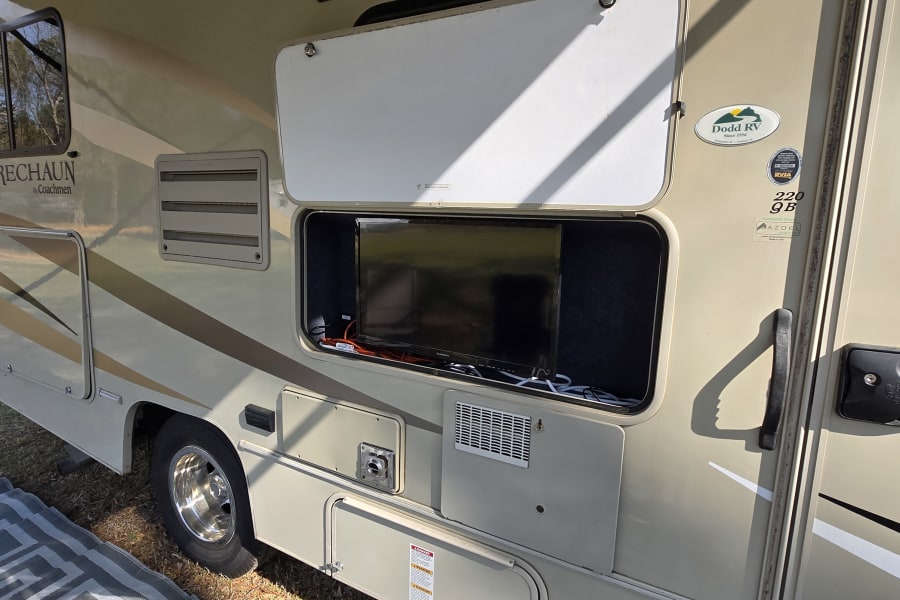 An RV rental shows an outdoor TV setup in an open storage compartment on the side, ready for camping entertainment.