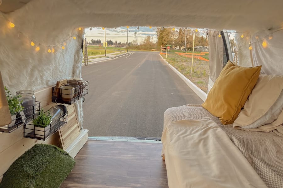 A comfortable rv rental interior, with a bed, shelves, and string lights, overlooks a quiet road.