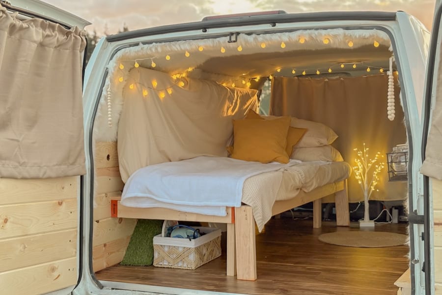 Cozy RV rental interior. A comfy bed, warm fairy lights, and wood accents create an inviting space for memorable travel.