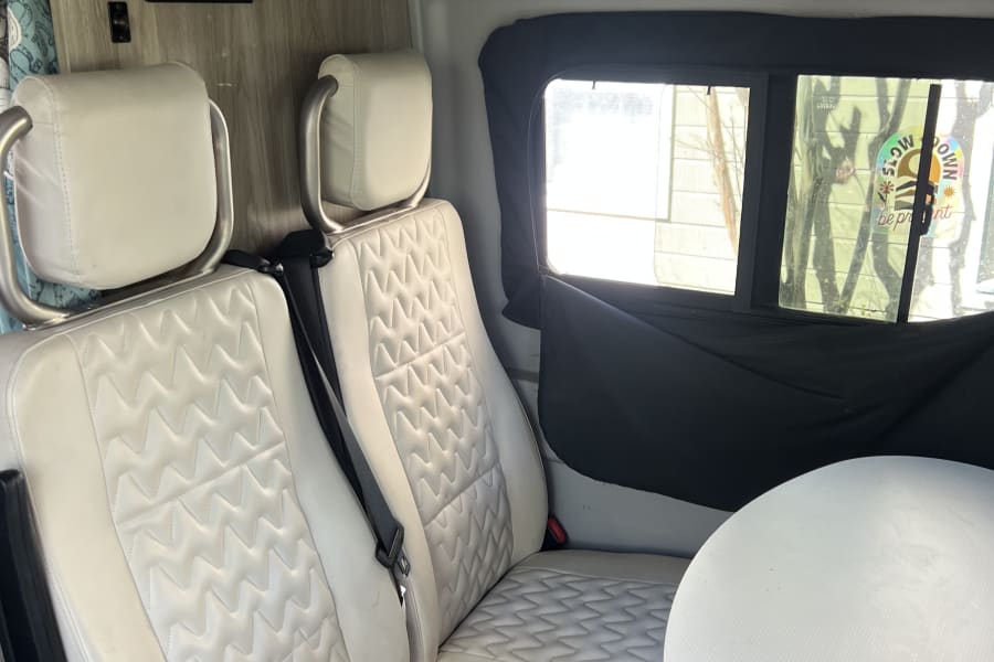 RV rental interior featuring quilted white seats, a dining table, and a control panel for solar and tank heater functions.